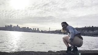 Girl squats by the water and pushes out a big shit