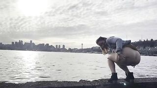 Girl squats by the water and pushes out a big shit