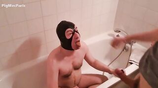 Woman in hood on knees licks shit off man in tub