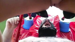 Man lays on his back in pink blanket while woman shits on his face
