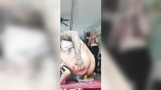 Woman with dyed hair and tattoos taking a shit in a plastic container